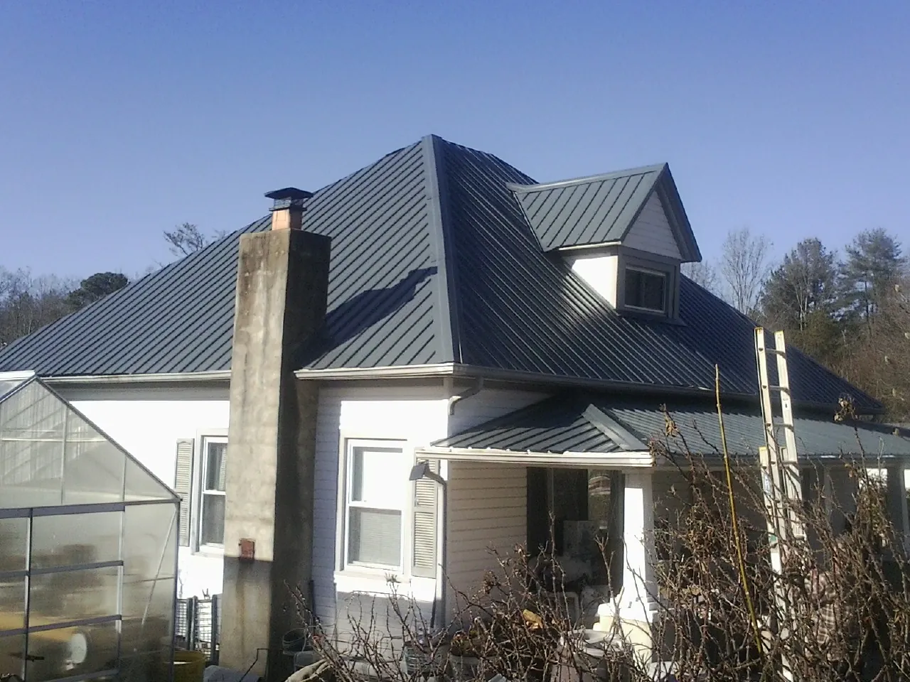 Dark blue standing seam metal roof on a white farmhouse with dormer — Slate & Tile Roof Repair by Roofing Brothers in Bronxville