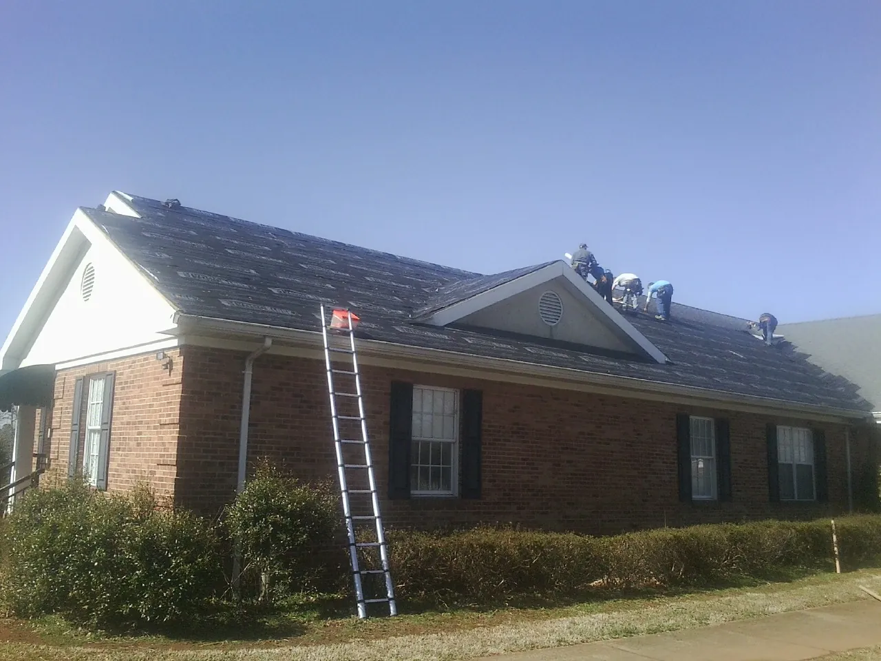 Crew tearing shingles off a brick ranch roof with a ladder set — Emergency Roof Repair work by our crew in Bronxville