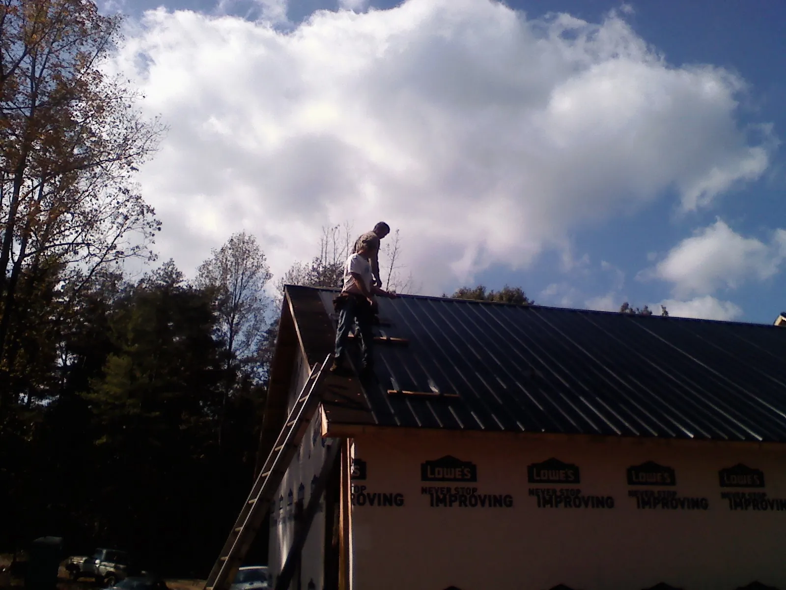 Roofer fastening dark metal panels high against a cloudy sky, from a Roof Inspection job in Bronxville