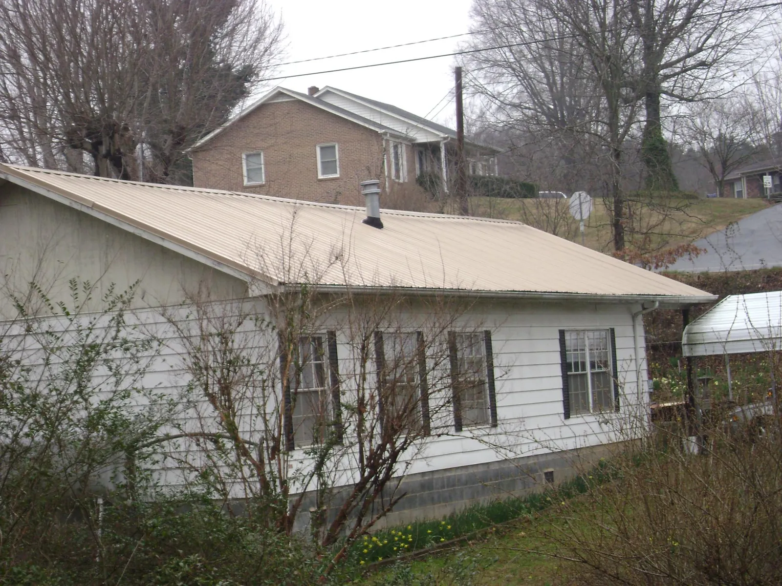 Tan metal roof on a white sided house set into a hillside — Commercial Roofing by Roofing Brothers in Bronxville